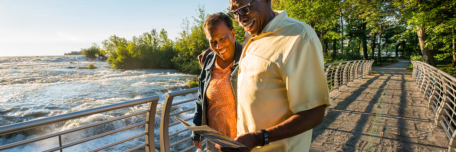 A couple reading a map walks along a paved path in Niagara Falls State Park near the Niagara River